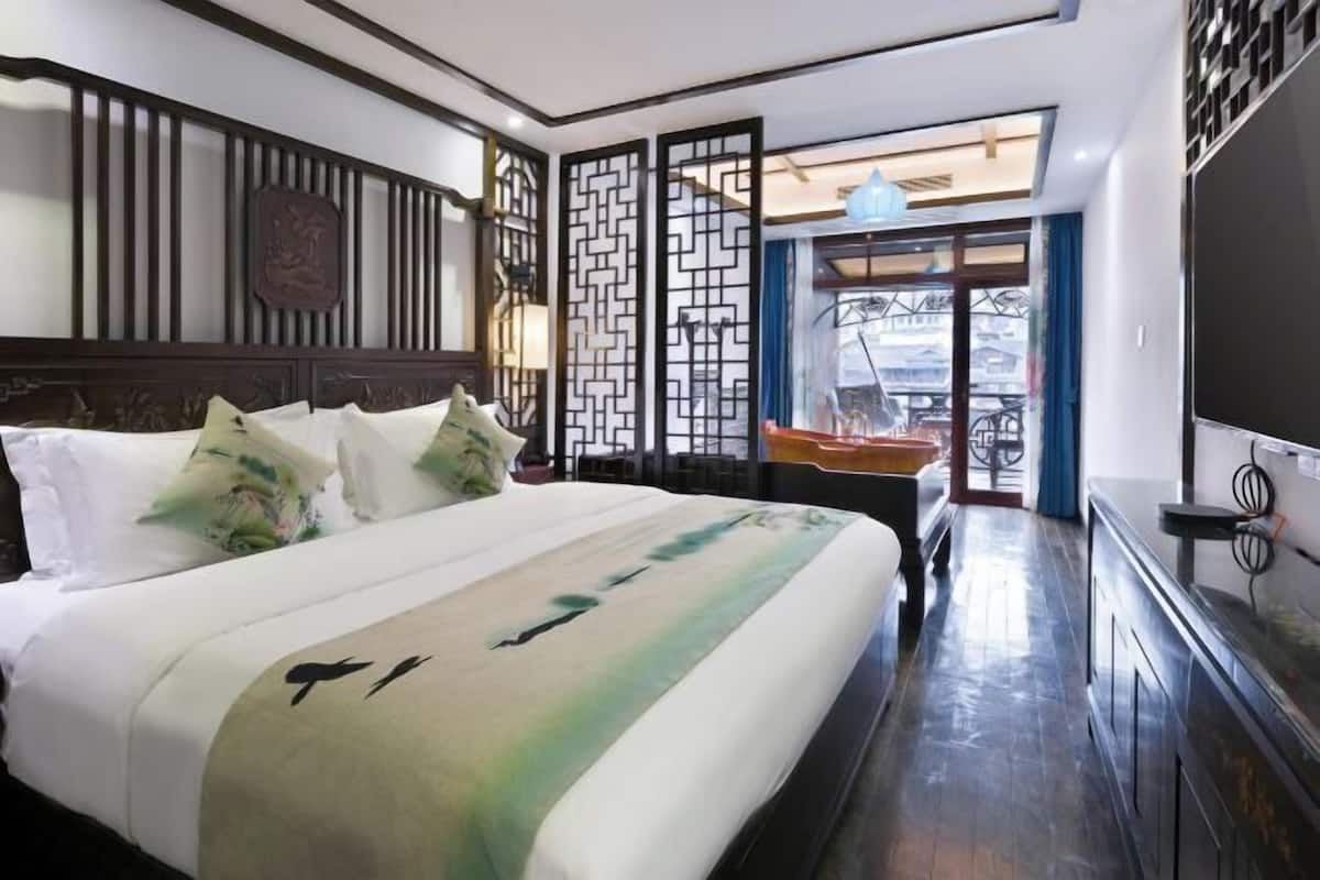 A hotel room with a bed, a TV, a desk, and a view of the outside.