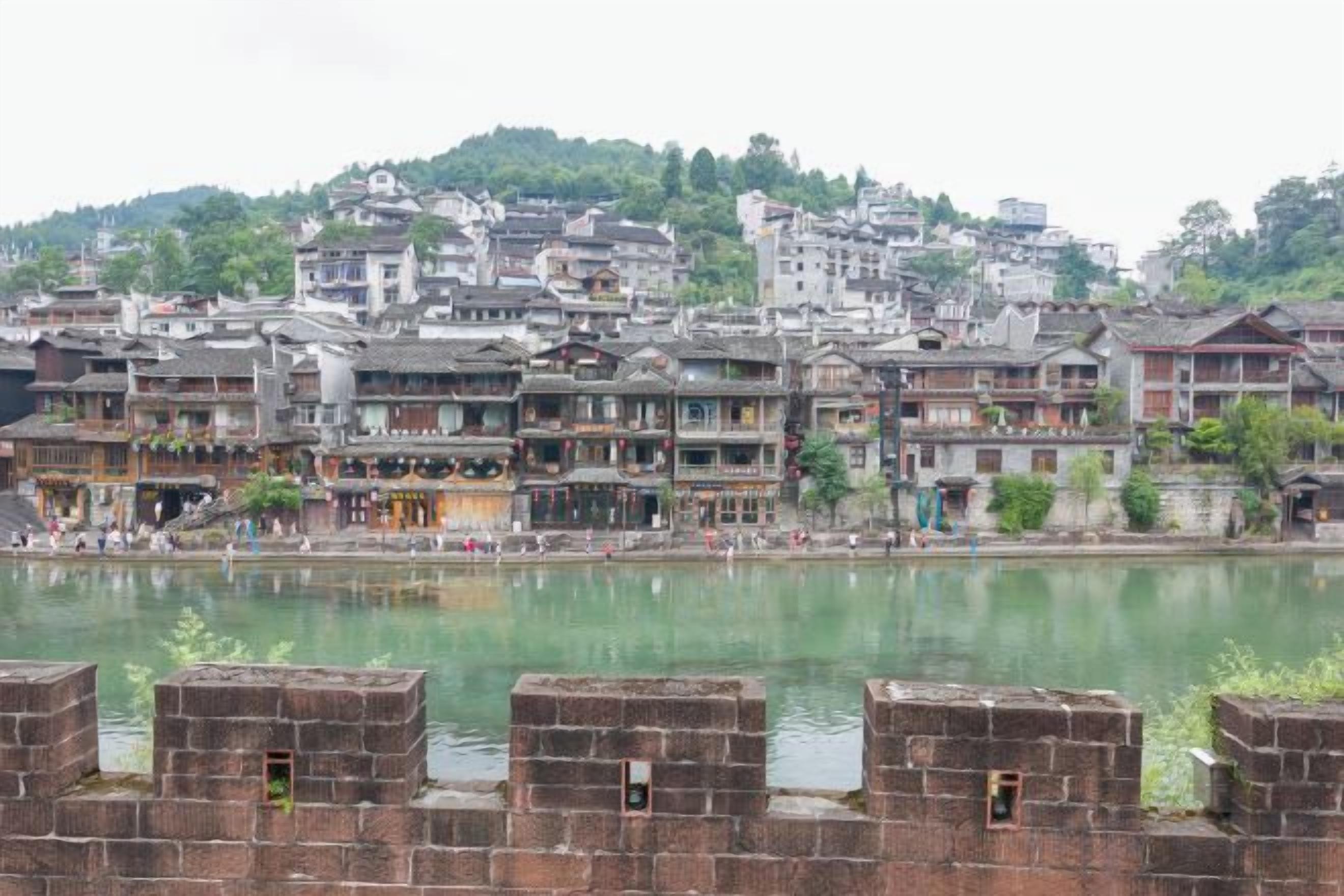 Une ville traditionnelle avec des bâtiments qui bordent une rivière, caractérisée par un mélange de styles architecturaux et par une étendue d'eau paisible au premier plan.