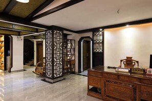 A traditional interior with a wooden reception desk, a decorative screen, and a staircase leading to another room. - Floral Hotel ·Fenghuang Grand Riverview (Fenghuang)