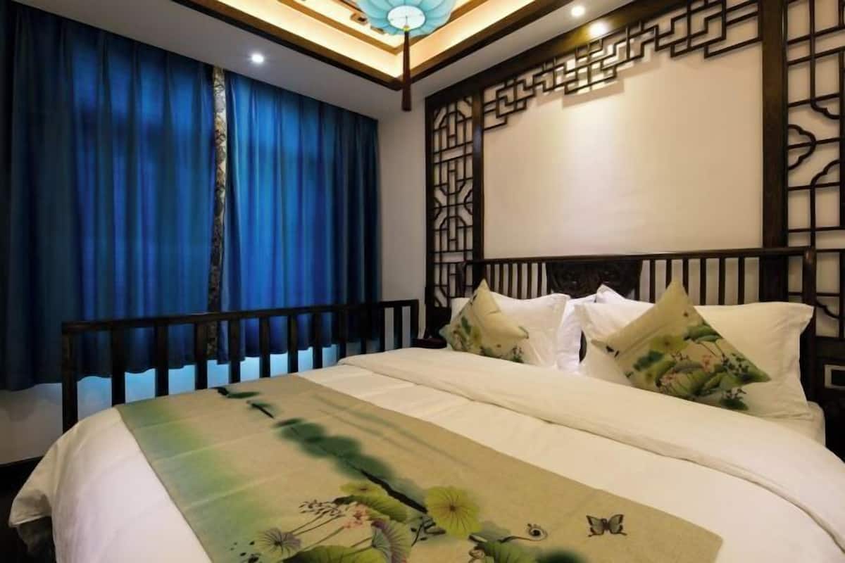A bedroom with a bed, curtains, a decorative headboard, and a ceiling light fixture.