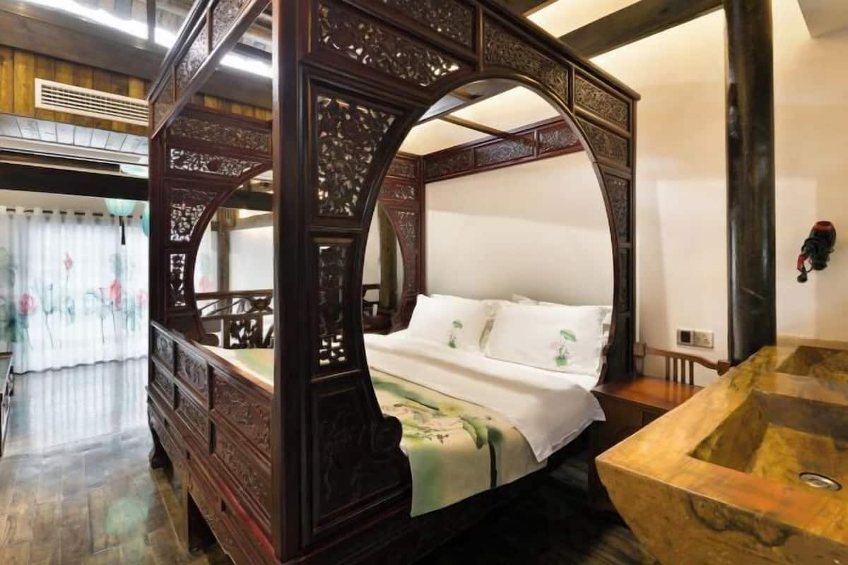 A traditional four-poster bed with intricate woodwork, a marble sink, and a wooden floor.