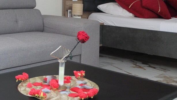 Una habitación moderna con un sofá gris, una mesita de centro negra con un adorno decorativo y una cama con almohadas rojas.