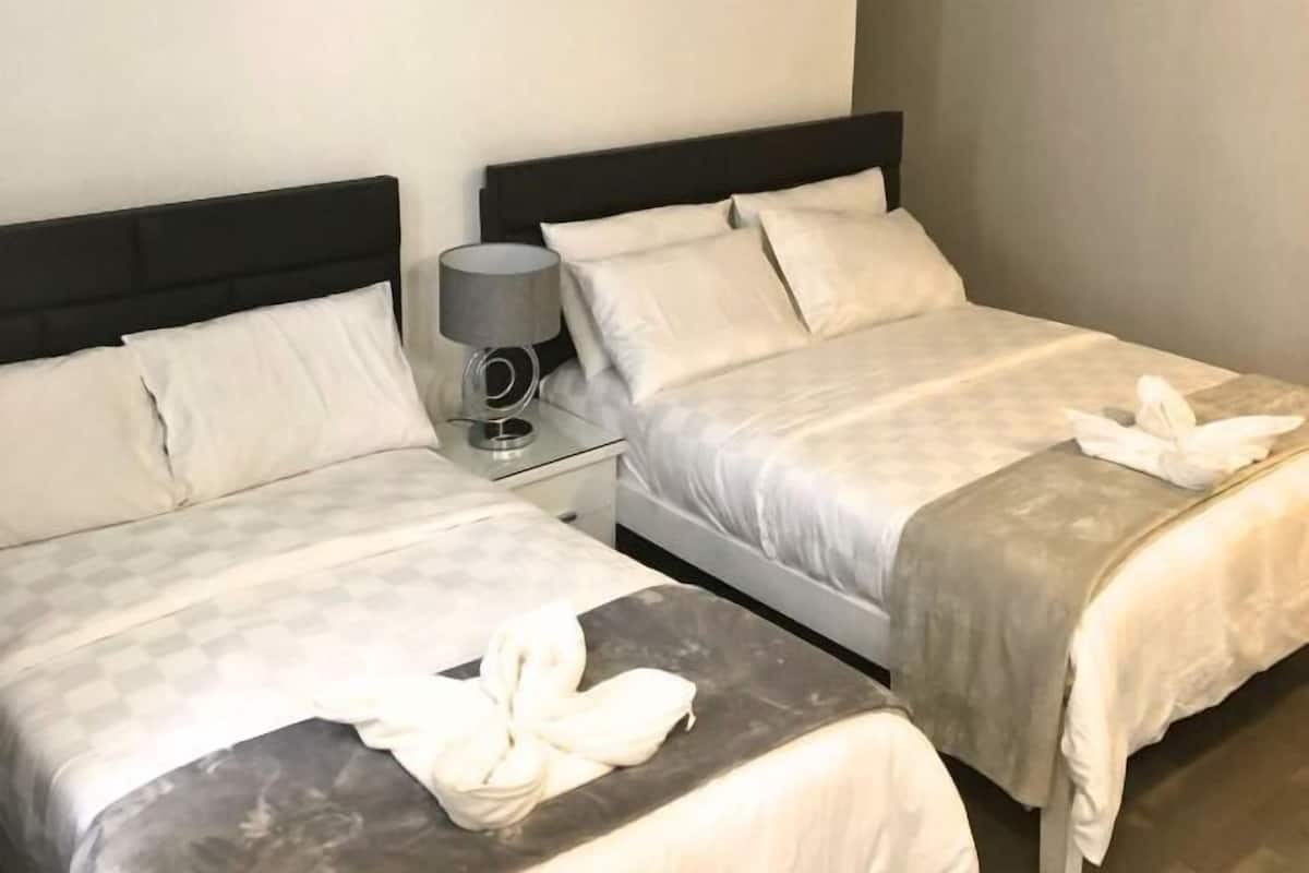 Two beds with white linens, a bedside table with a lamp, and a towel on the floor.