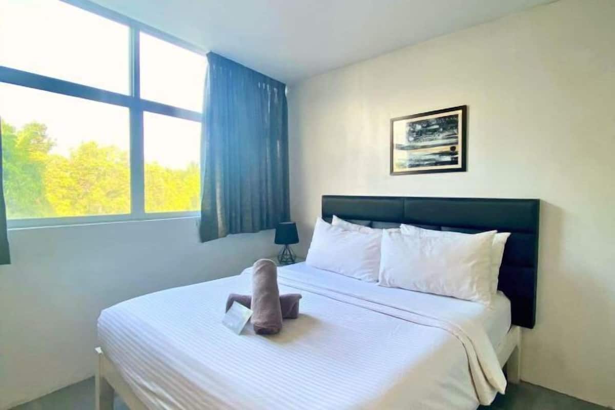 A hotel room with a large bed, a headboard, a window with curtains, and a framed picture on the wall.