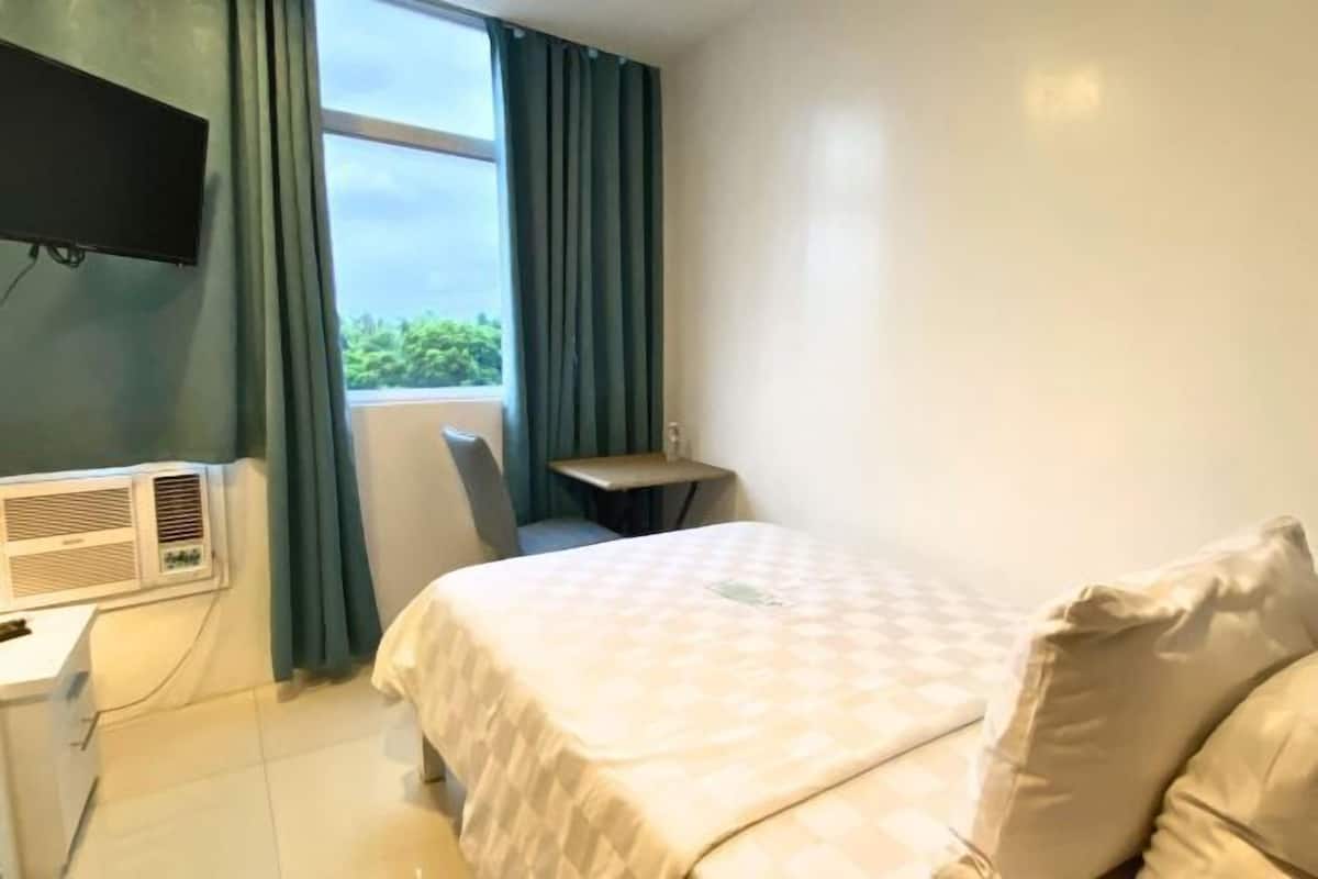 A hotel room with a bed, a desk, a chair, a TV, and a window with curtains.