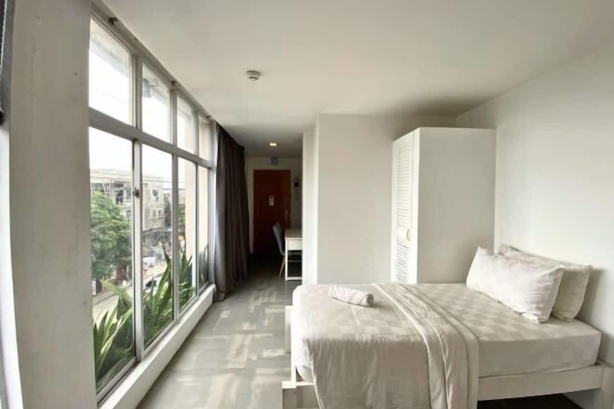 A bedroom with a large window, a bed, and a wardrobe.