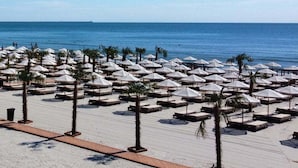 A beach with rows of sun loungers and umbrellas, palm trees, and a clear view of the ocean. - Apartamente Stefan Resort 4 (Mamaia-Sat)