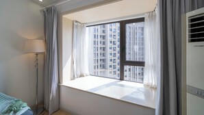Een kamer met een groot raam, een staande lamp en een airconditioning.