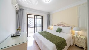 Een hotelkamer met een bed, nachtkastjes, een bureau van glas, een raam met gordijnen en een airconditioning.