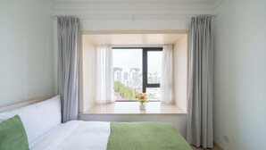 Een hotelkamer met een groot bed, een raam met gordijnen en uitzicht op gebouwen.