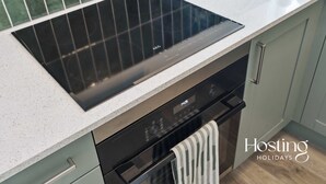 A modern kitchen with a black induction cooktop, a built-in oven, and a stainless steel range hood. - Old Bell Annexe - Cosy 1Bed Stay in Central Henley (Henley-on-Thames)