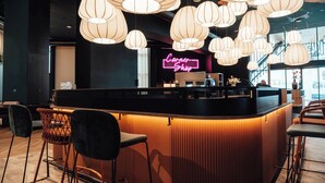 A modern bar area with a neon sign, multiple hanging pendant lights, and a counter with bar stools. - Ecla Genève Archamps (Archamps)