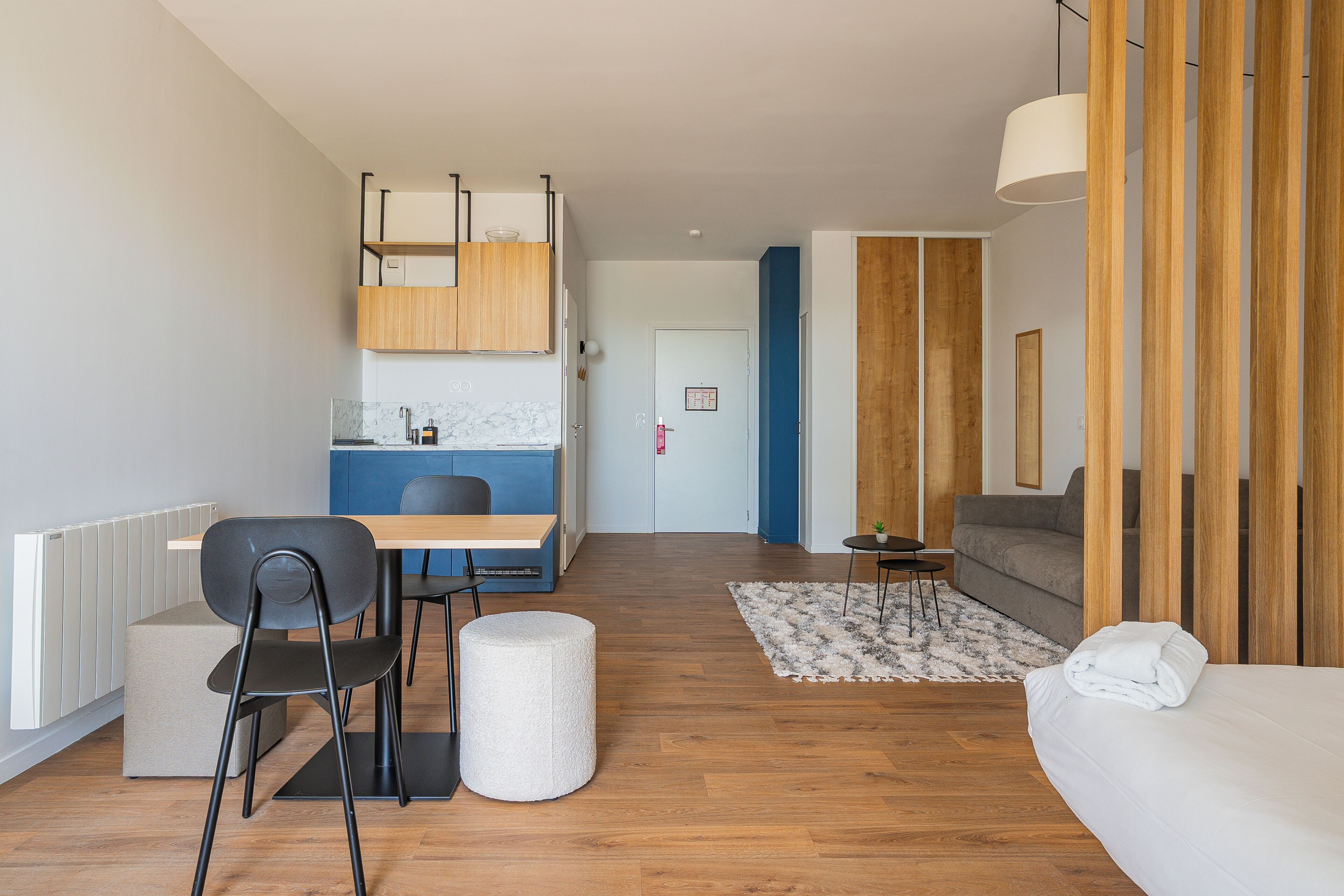 Una habitación de hotel moderna con piso de madera, una cama, un sofá, un área de comedor con mesa y sillas, y una cocina.
