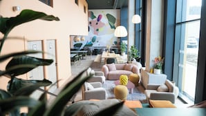 A modern hotel lobby with a large dining area, comfortable seating, and large windows. - Ecla Genève Archamps (Archamps)