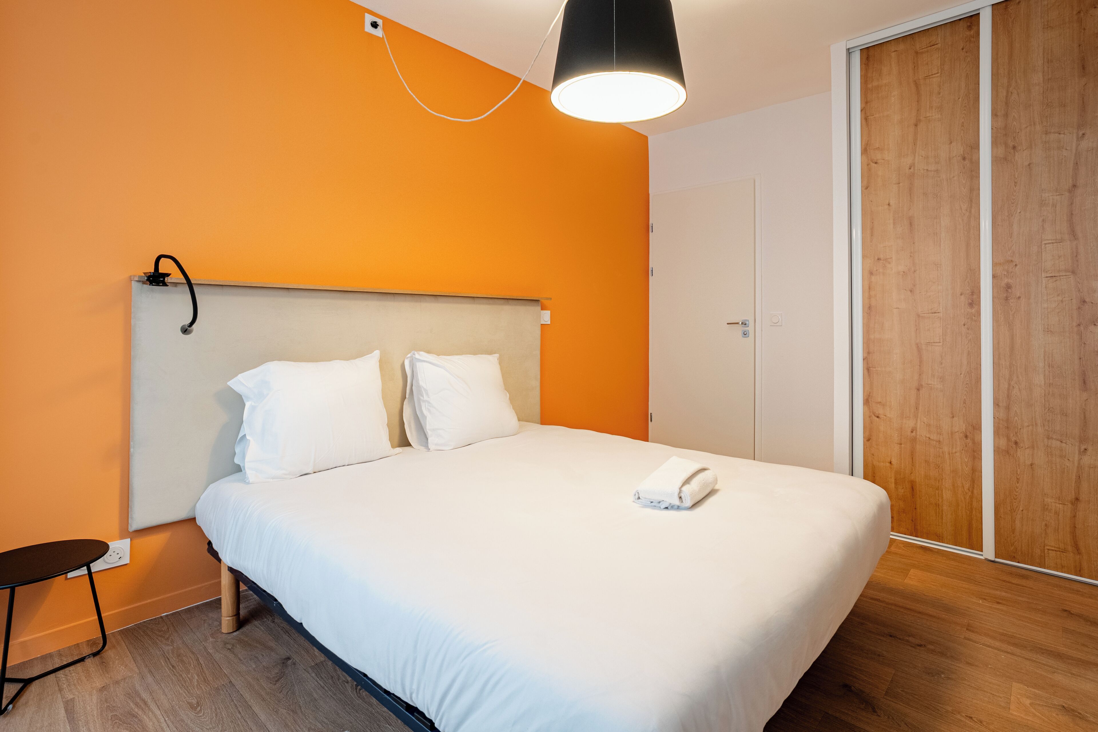 Una habitación de hotel con cama, mesita de noche, lámpara colgante y armario de madera.