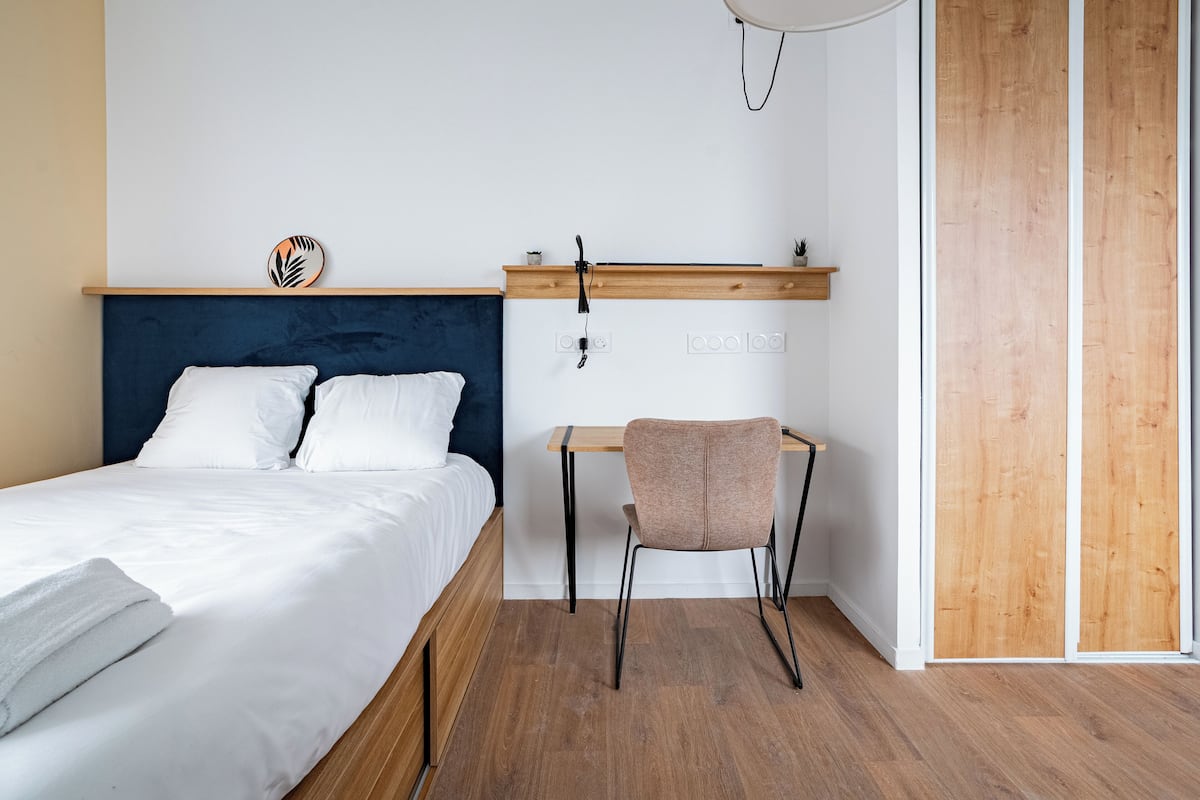 Een slaapkamer met een bed, een bureau, een stoel en een houten garderobe.