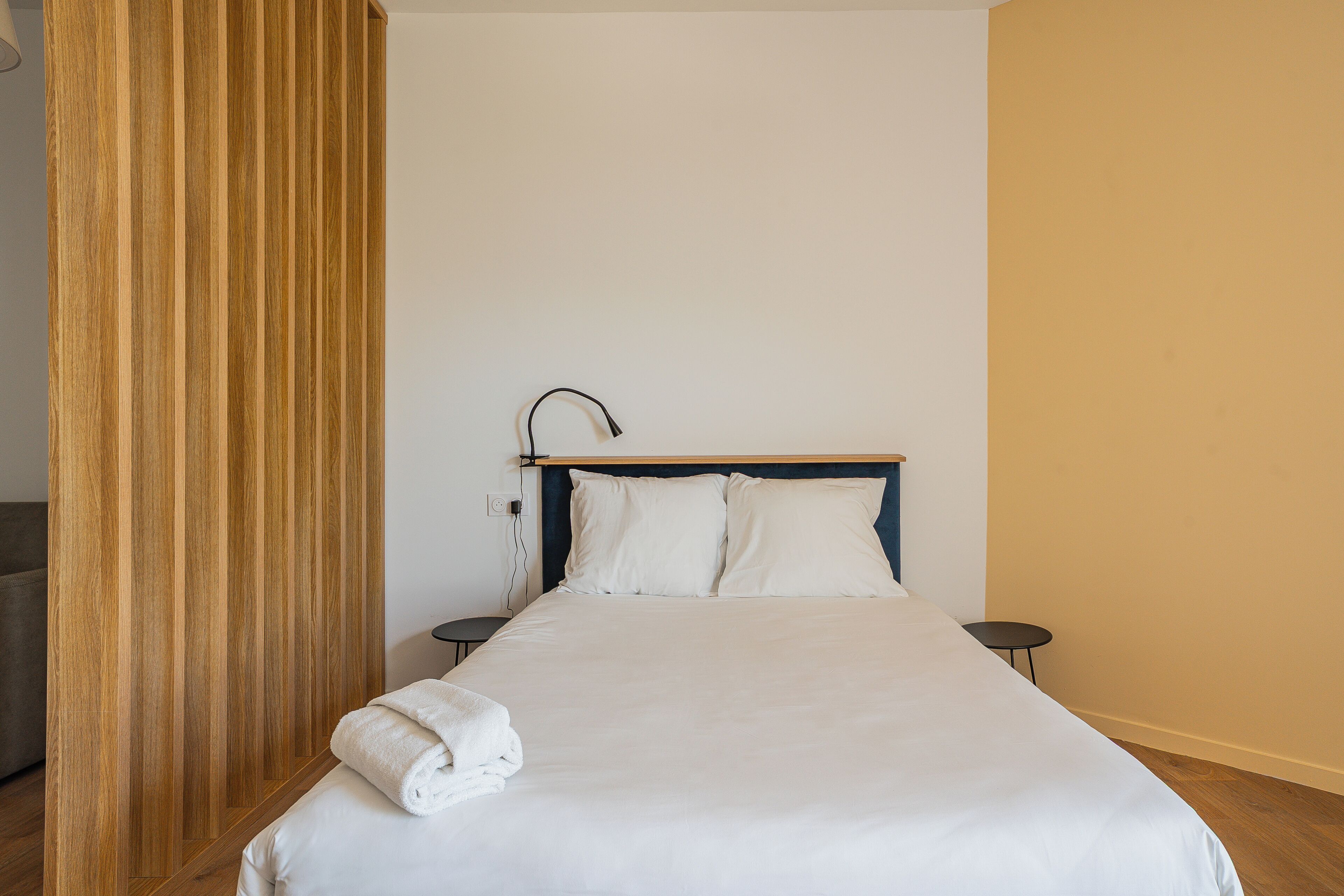 A neatly made bed with white linens, a wooden headboard, and a small bedside table.