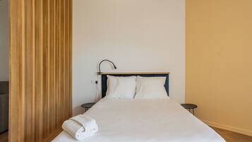 A neatly made bed with white linens, a wooden headboard, and a small bedside table.