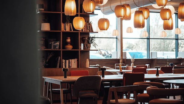 A restaurant with wooden furniture, pendant lights, and a bookshelf with books and decorative items. - Ecla Genève Archamps (Archamps)