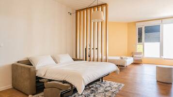 A bedroom with a bed, a chair, a sofa, a window, and a view of the outdoors.