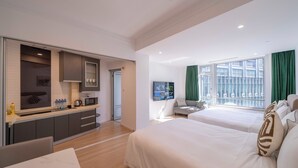 Une chambre d’hôtel moderne dotée d’un coin cuisine, de deux lits, d’une table à manger et d’une grande fenêtre avec des rideaux.