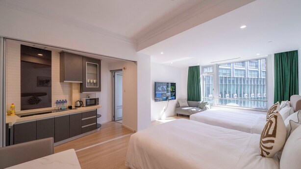 A modern hotel room with a kitchen area, two beds, a dining table, and a large window with curtains. - Tyms Xuhui Spacious 1BR APT  (Shanghai)
