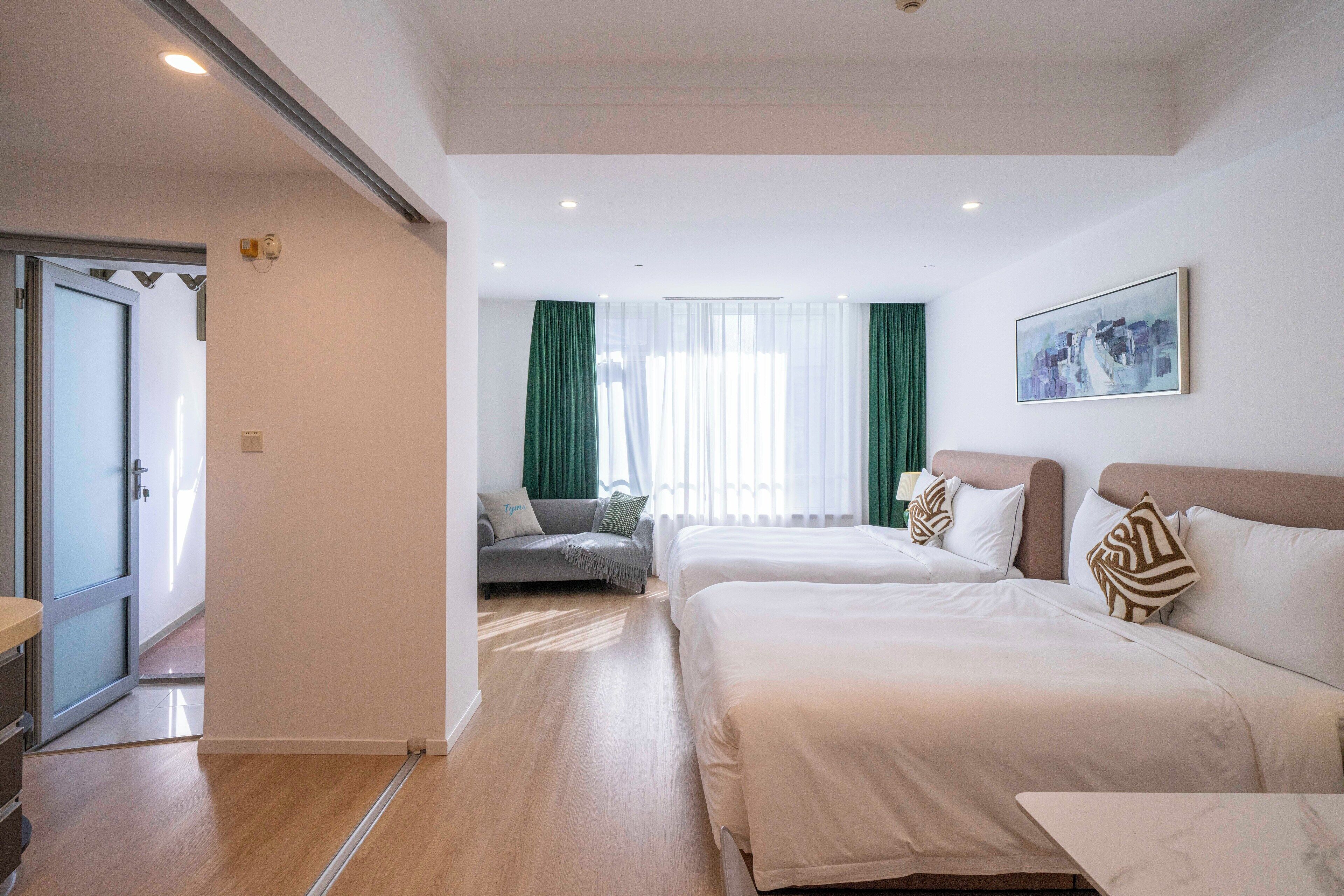 A hotel room with two beds, a sofa, a dining table, and a large window with curtains.