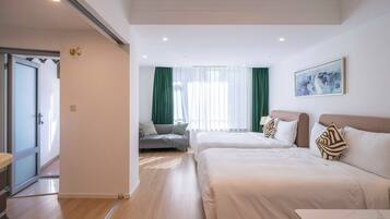 A hotel room with two beds, a sofa, a dining table, and a large window with curtains.