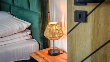 Un lit bien fait, avec une tête de lit verte, une table de chevet en bois surmontée d’une lampe en osier et une porte en bois dotée d’une poignée noire.