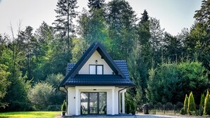 A small, modern house with a triangular roof, surrounded by a well-maintained lawn and dense forest. - Domki Perła Białki z Jacuzzi (Bukowina Tatrzanska)