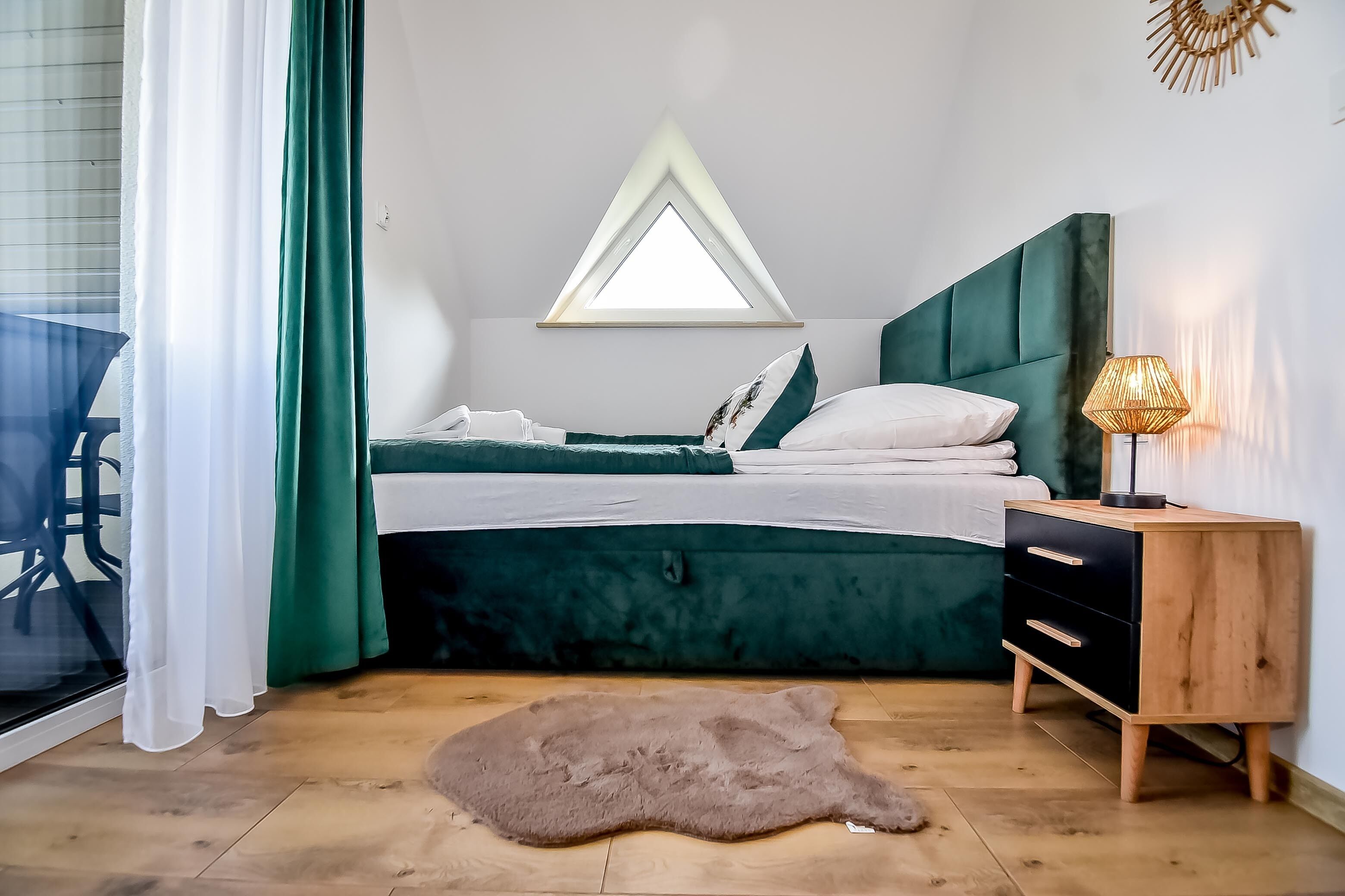 A bedroom with a bed, a nightstand, a window, and a fur rug.