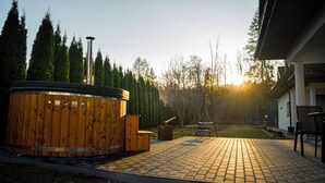 A wooden hot tub with a metal pole, a brick patio, and a building in the background. - Domki Perła Białki z Jacuzzi (Bukowina Tatrzanska)