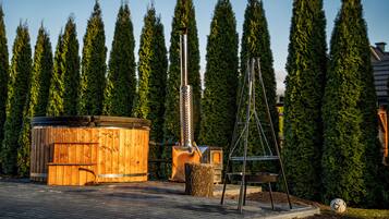 A wooden hot tub, a metal structure, and a soccer ball on a paved area with tall trees in the background.