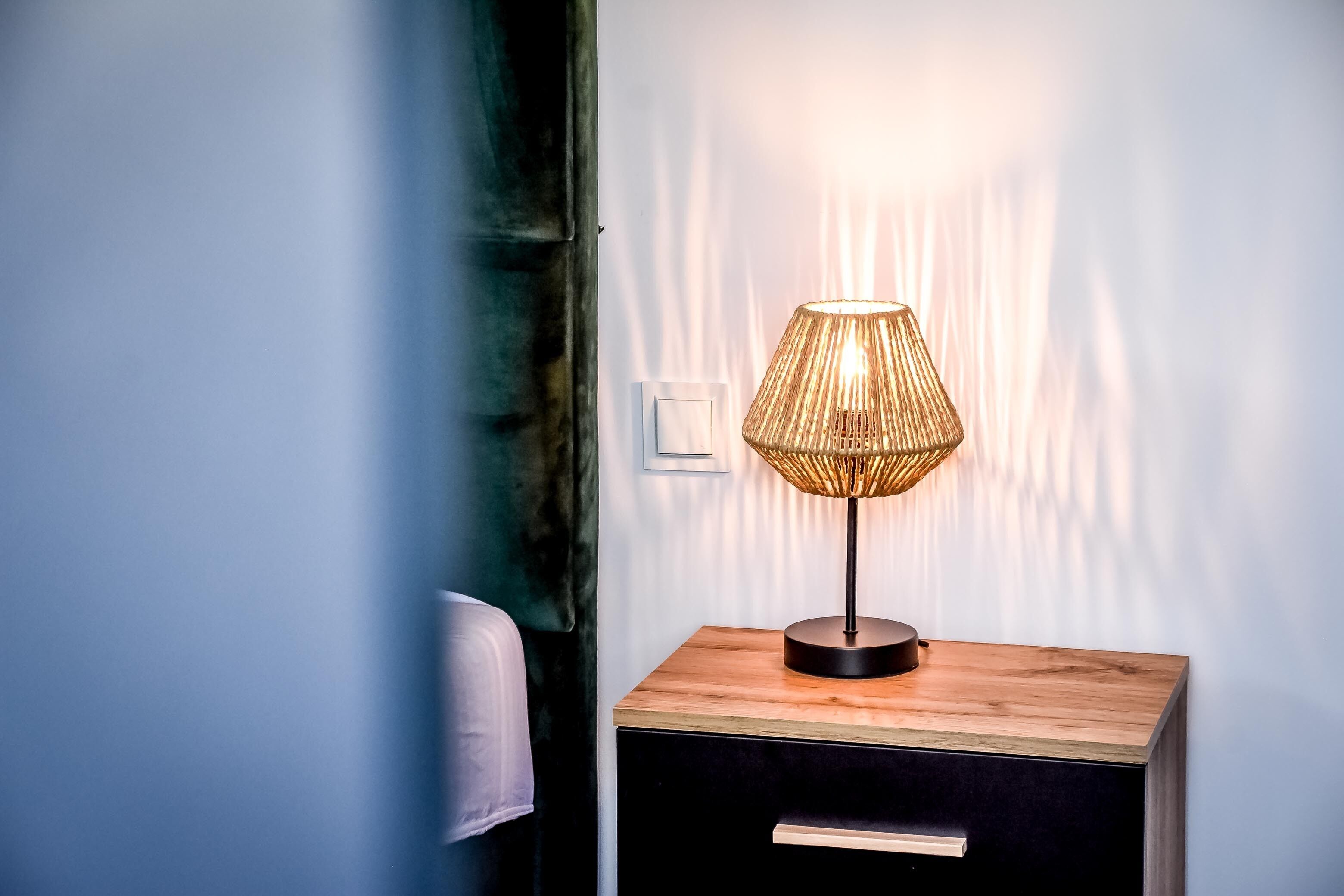A bedside table with a lamp, a drawer, and a switch on the wall.