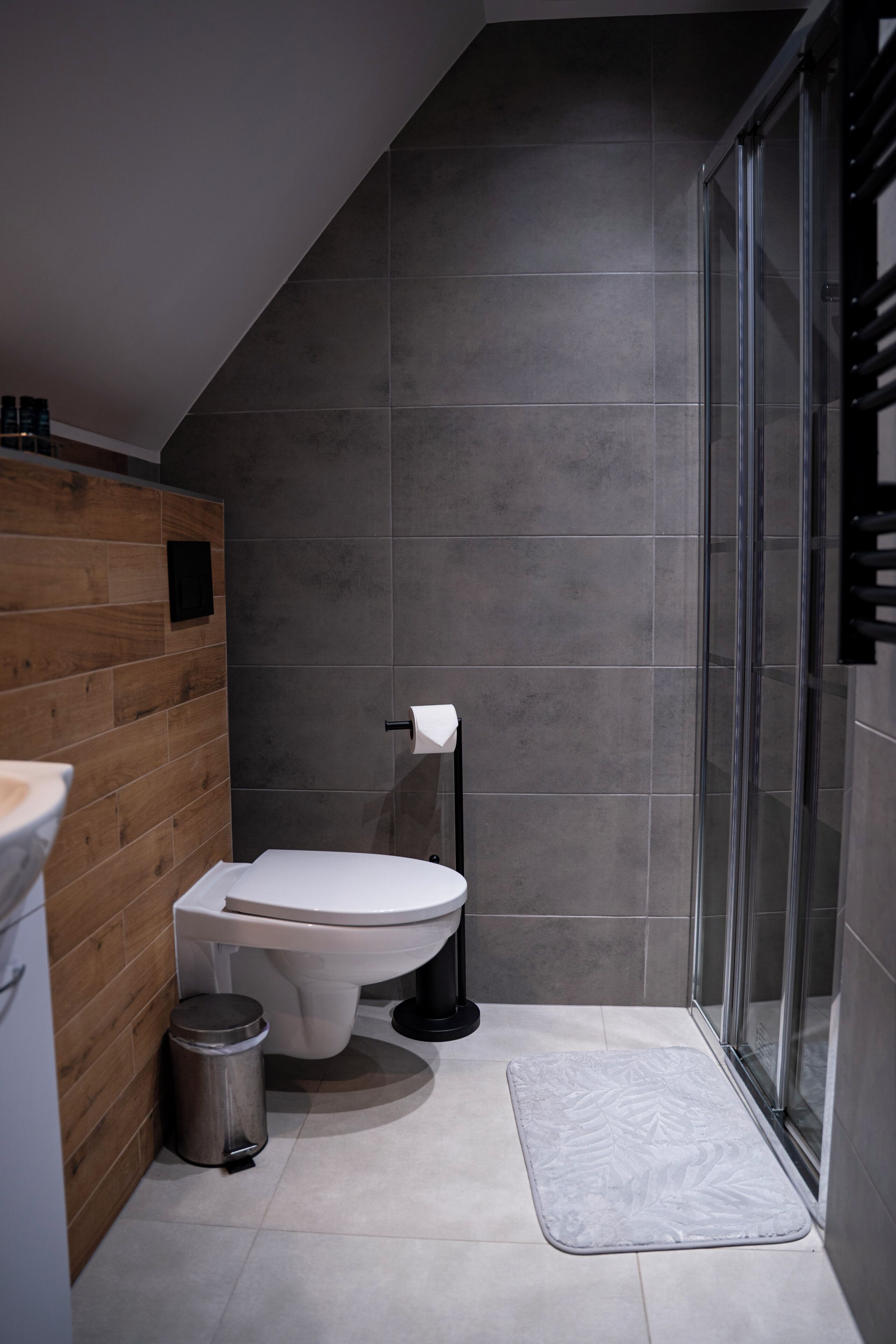 Une salle de bain moderne comprenant des toilettes, une poubelle, un espace douche et un mur d’accent en bois.