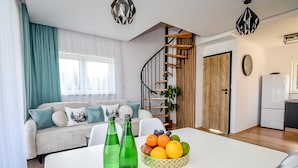 A modern living room with a sofa, a dining table with fruit and bottles, a staircase, and a kitchen area. - Domki Perła Białki z Jacuzzi (Bukowina Tatrzanska)