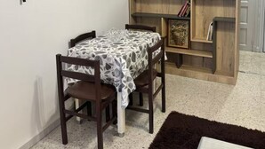 A compact living space with a dining table and chairs, a TV mounted on the wall, a wooden bookshelf, and a door in the background. - Urban Oasis in Algiers' Heart (Sidi M'Hamed)