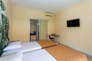 A hotel room with two beds, a desk, a chair, a TV, and a sliding door leading to a bathroom. - Cove Kanaya (Bali)