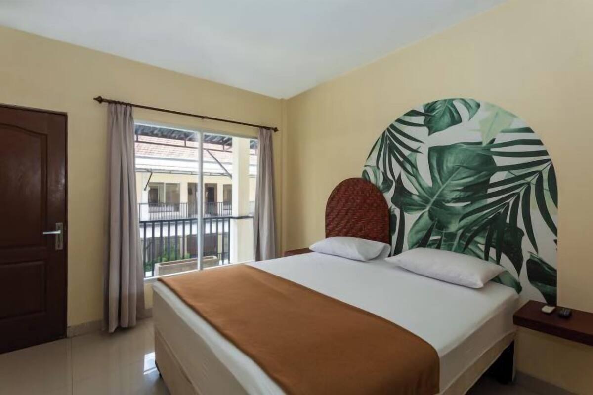 A hotel room with a bed, a view of the outside, a door, and a nightstand.