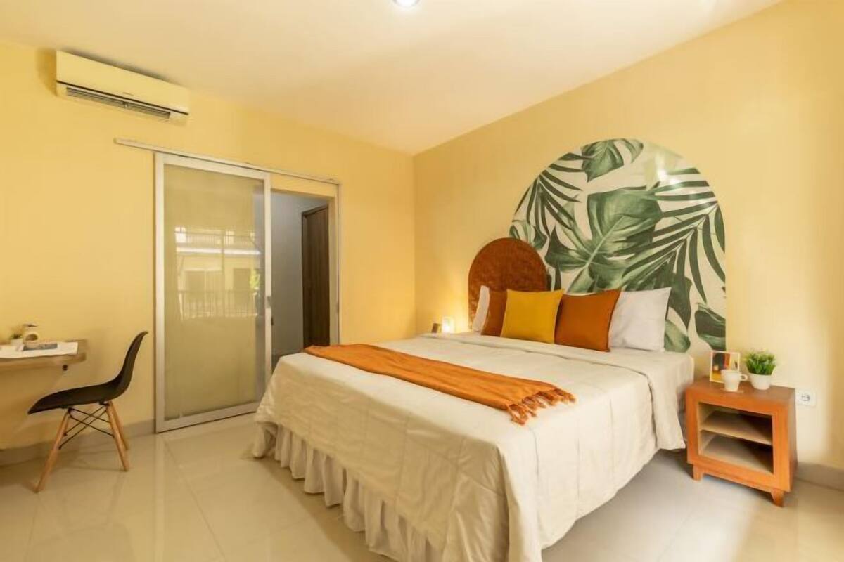 A bedroom with a bed, a desk, a chair, a nightstand, and a large wall mural.