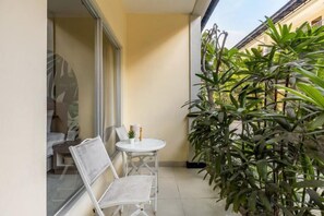 A small balcony with a white table and chairs, a potted plant, and a view of the building's exterior. - Cove Kanaya (Bali)