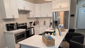 Una cocina moderna con armarios blancos, electrodomésticos de acero inoxidable y una isla central con taburetes de bar.