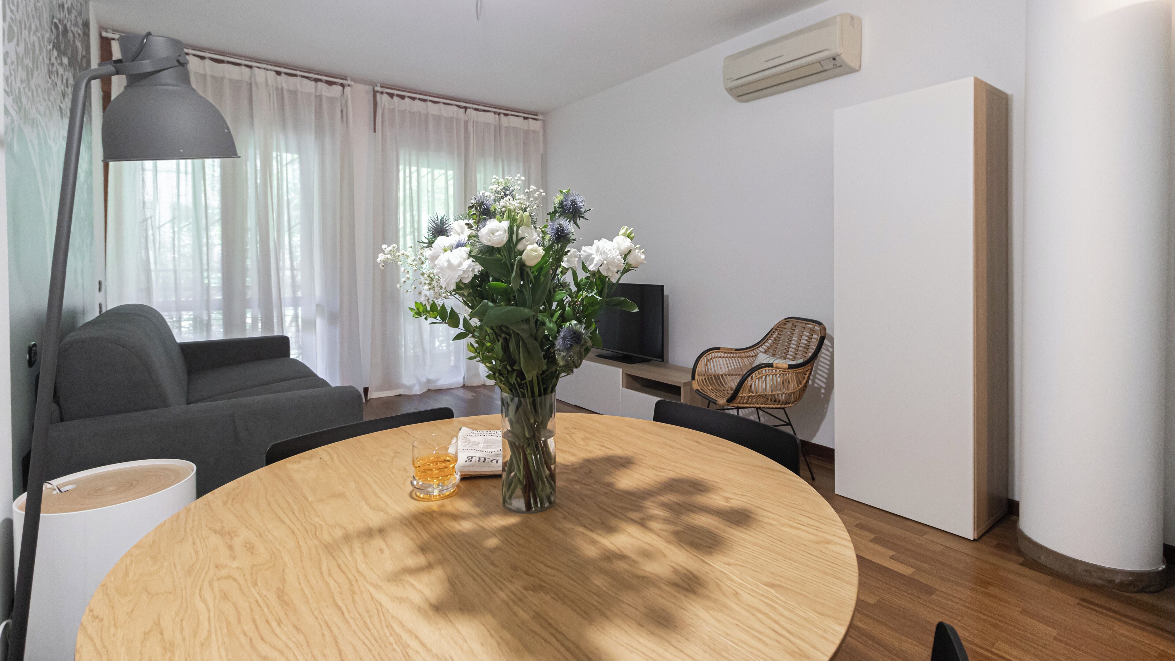 Ein modernes Wohnzimmer mit einem runden Holztisch, einer grauen Couch und einem Fernseher auf einem Schrank.