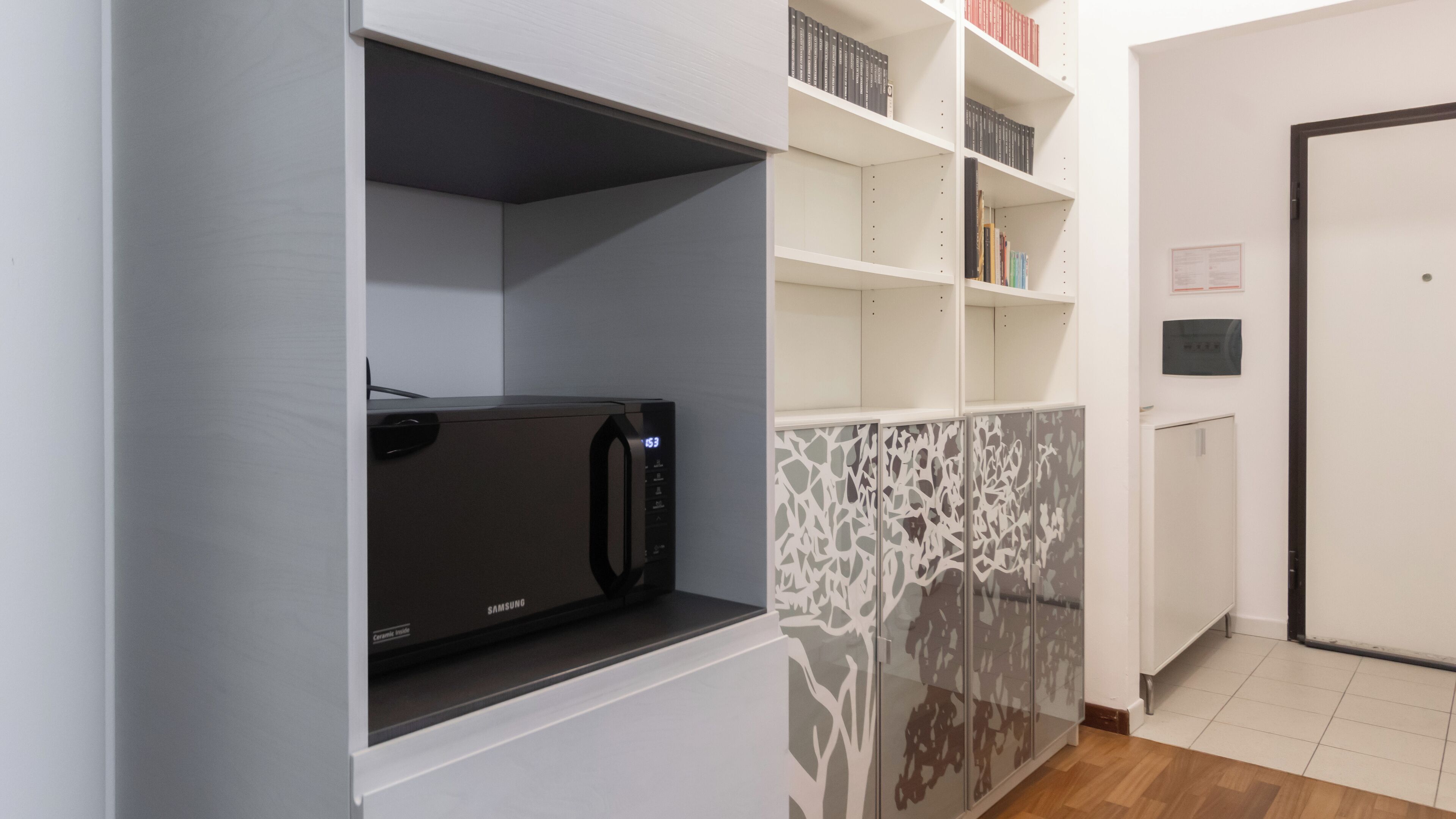 A kitchen with a microwave, white cabinets, and a patterned glass door.