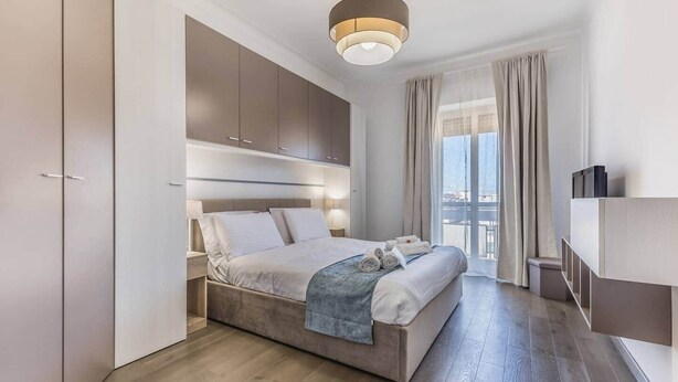 A modern bedroom with a large bed, built-in wardrobe, and a view of the city. - St. John Lateran (Rome)
