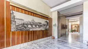 A hallway with a marble floor, a wooden panel with a black and white cityscape mural, and a potted plant. - St. John Lateran (Rome)
