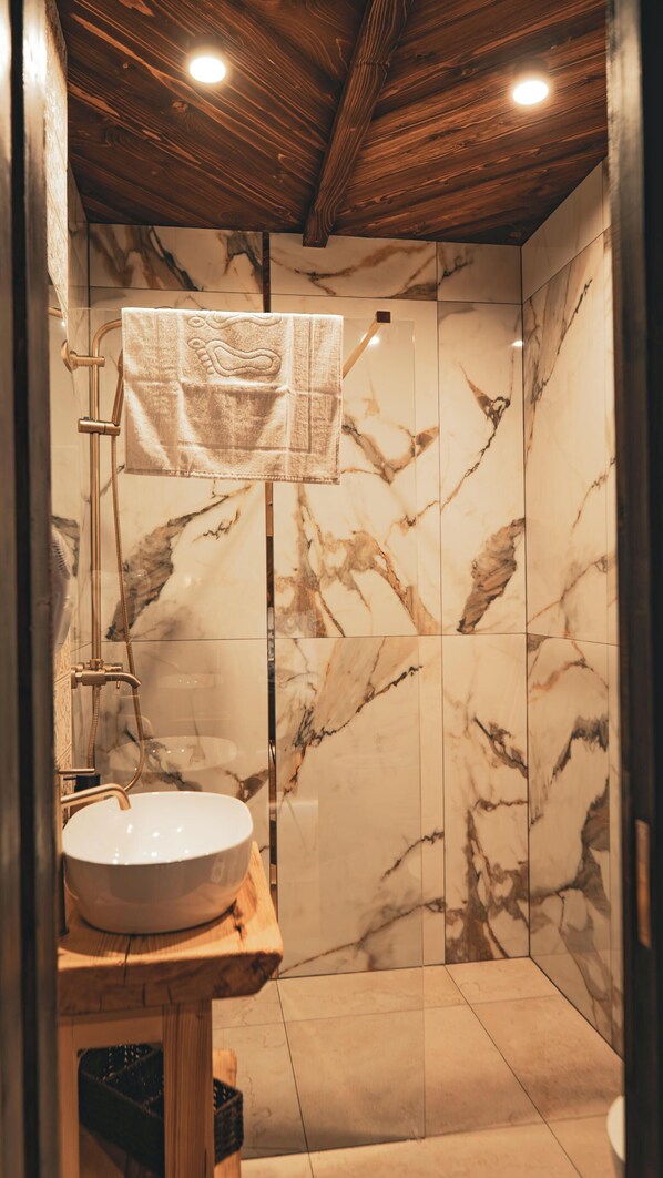 Une salle de bain avec un mur de douche en marbre, un plafond en bois et un lavabo sur lequel est posée une serviette, suspendue à un porte-serviettes.