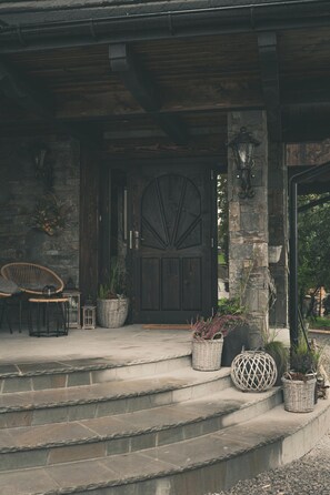 A stone staircase leading to a wooden door with a fan-shaped design, surrounded by wicker baskets and potted plants. - Highland Apartments Pod Gubałówką (Poronin)