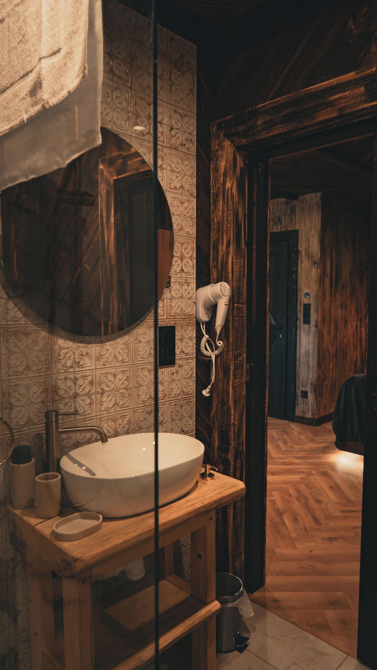 Un baño con un lavabo grande y redondo, un secador de pelo fijado en la pared y un mueble de tocador de madera.