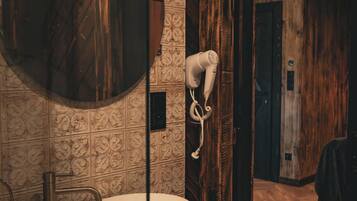 Un baño con un lavabo grande y redondo, un secador de pelo fijado en la pared y un mueble de tocador de madera.